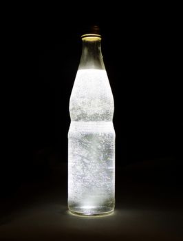 Cold mineral water with gas bubbles on a black background. Beautiful glass bottle close-up.