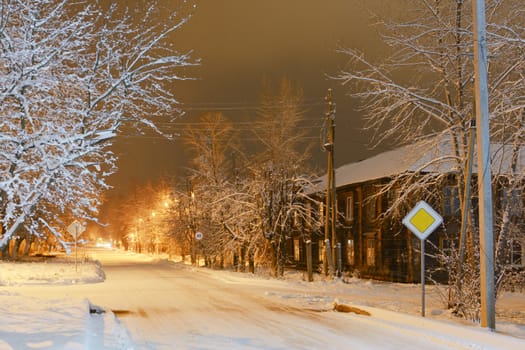Old wooden house on a snowy frosty street in night illumination
