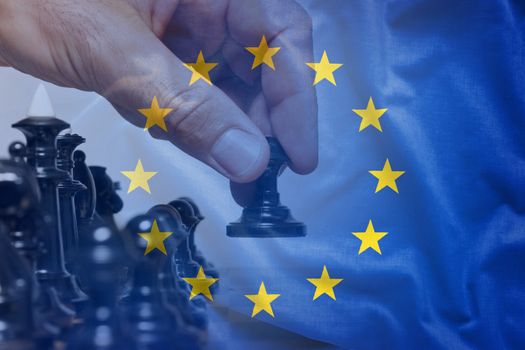 European Union flag chess move concept with hand of chess player viewed behind half-transparent fabric, making a first move with black pawn