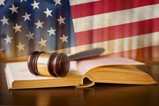 Law enforcement and the judiciary in the United States with a composite image of a judges gavel on a law book in the courtroom against the Stars and Stripes national flag