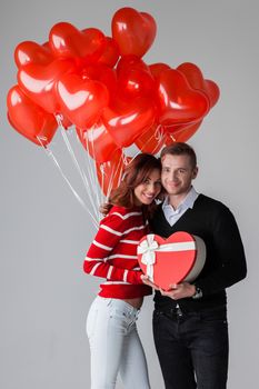Happy smiling couple holding valentines day gifts and red balloons on white background