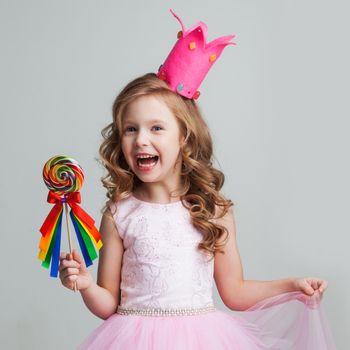 Beautiful little candy princess girl in crown holding big lollipop and smiling