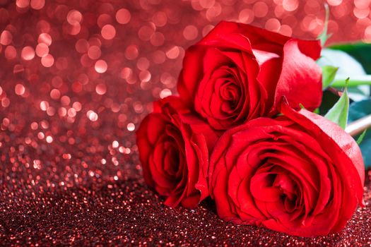 Three red roses over bokeh glittering background