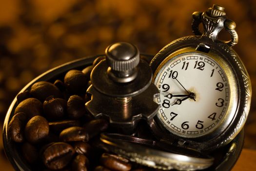 Coffee bean and pocket watch the tray of manual grinder on table. Closeup and copy space. Concept of coffee time in morning.