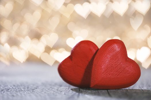 Two small handmade red wooden hearts on bright golden lights bokeh background Valentines day card