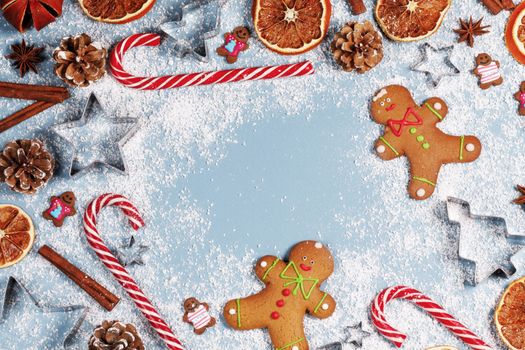 Christmas food gingerbread cookie caramel candy cane cinnamon mold shape anise orange slice on blue background with copy space
