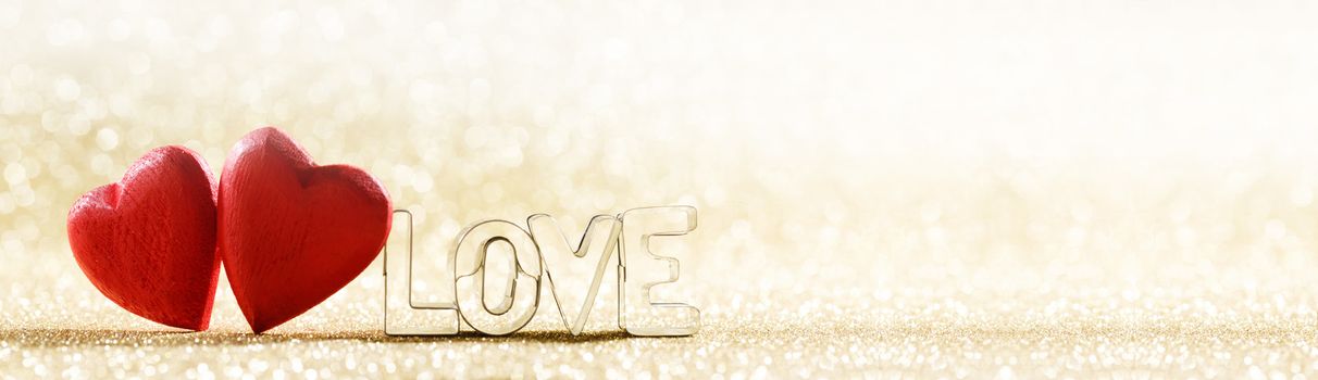 Two red handmade wooden hearts and word love on golden bright glitter lights bokeh background