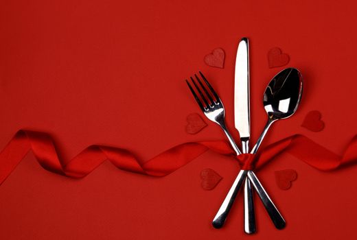 Cutlery set tied with silk ribbon and hearts on red background Valentine day dinner concept