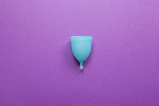 Turquoise menstrual cup on purple background. Concept zero waste living, savings, minimalism, these days. Feminine hygiene product, flat lay, copy space. Horizontal.