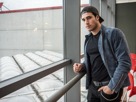 Attractive young man indoors wearing a denim jacket and baseball cap, reversed