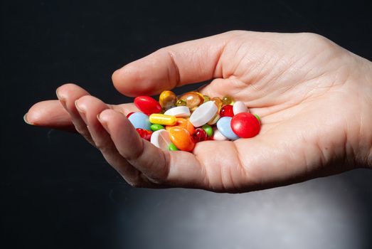 Different coloured drugs in a woman's hand on a glass background