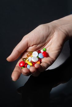 Different coloured drugs in a woman's hand on a glass background