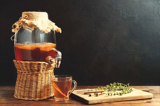 Fresh homemade Kombucha fermented tea drink in jar with faucet and in cup on dark background.