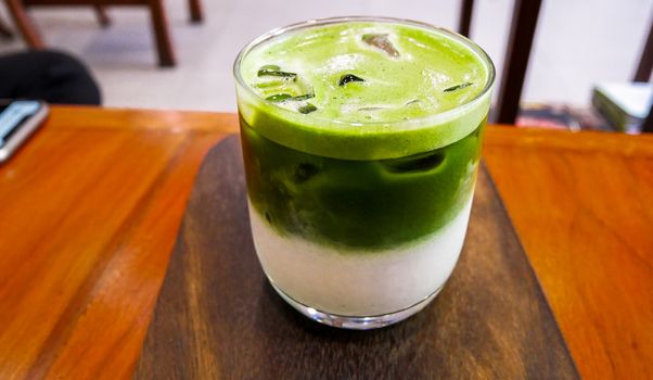 Green tea glass cup with milk ice and heart shape. cool green tea in the glass cup with heart pattern on the wooden table. Beverage, full. Wood texture,