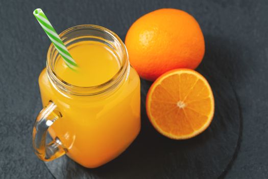 Homemade freshly squeezed orange juice in a Masonic jar and oranges on a black background.