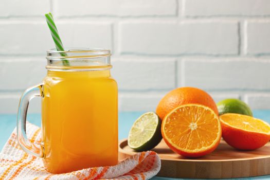 Homemade freshly squeezed orange juice in a mason jar, oranges and lime on wooden dish closeup, copyspace.