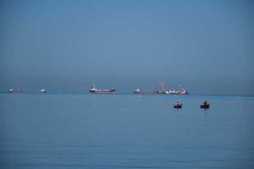 The Small Fisherman Boat in the Sea. A small fisherman boat floating on the sea near the seashore with Cargo ship background