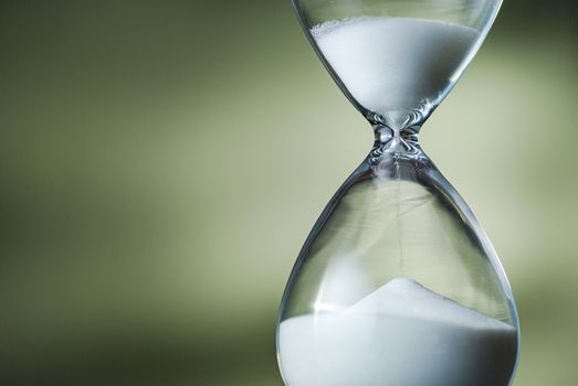 Sand running through the bulbs of an hourglass or egg timer in a concept of countdown, urgency, passing time and deadlines on green with copy space