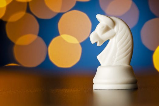 White horse chess piece on a wooden table over a colorful bokeh effect of golden light in a conceptual image