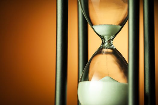 Close up on an hourglass with running sand over a coppery background with copy space conceptual of a countdown, deadline, or time management