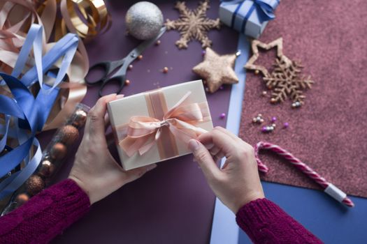 Female hands holding present gift for Christmas. Top view at workplace for preparing handmade decorations. with color paper glitters baubles balls decorative stars ribbons