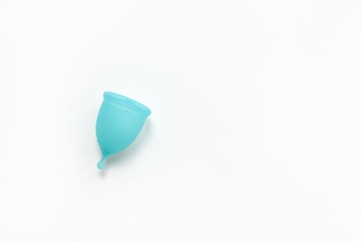 Turquoise menstrual cup on white background. Concept zero waste, savings, minimalism, environmental conservation, sustainable lifestyle. Feminine hygiene product, flatlay, copy space. Horizontal.