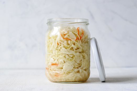 Transparent jar filled with juicy sauerkraut composed on white background