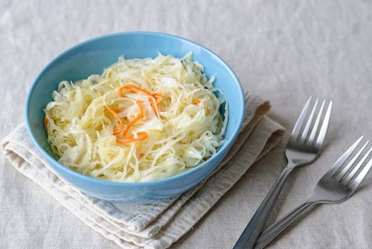 From above of served blue bowl filled with juicy salted cabbage on napkin on table