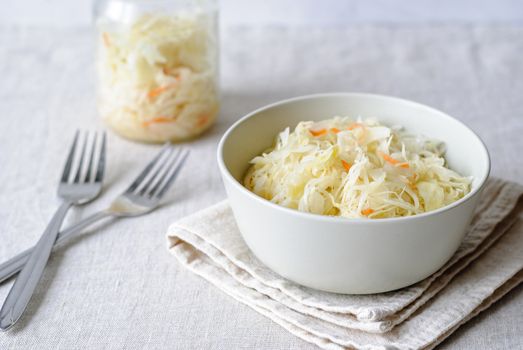 Closeup of white bowl with juicy sauerkraut served on napkin with forks