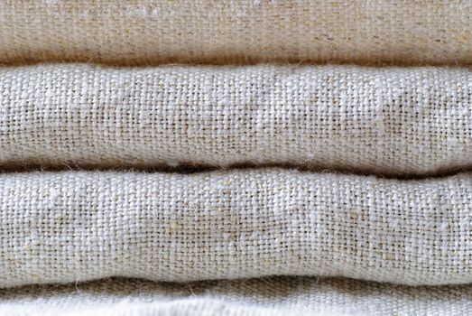 Neatly folded woven linen fabric in a neutral shade stacked on top of one another in a close up full frame background