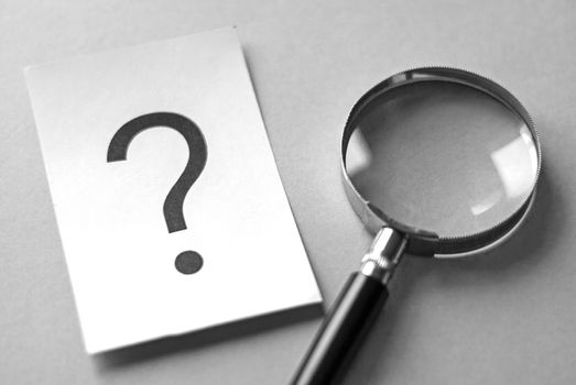 A question mark and a magnifying glass on a gray background, the concept of finding the answer to the question.