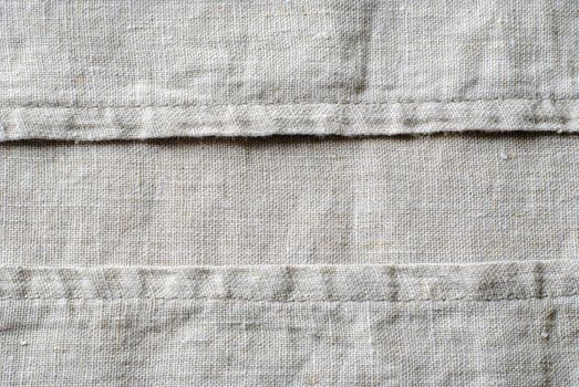 Woven linen fabric showing the stitching on the seams arranged neatly in parallel lines in a close up full frame view