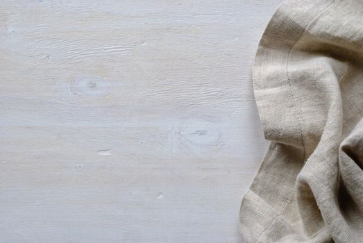 Folded and gathered linen fabric side border in a neutral weave over textured white painted wood with copy space