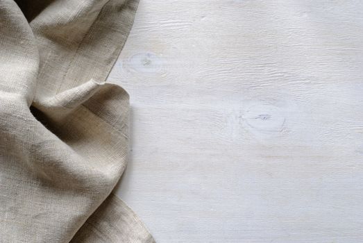 Folded gathered border of a natural linen fabric showing the detail of the weave over textured painted white wood boards with copy space