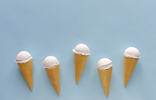 Row of five vanilla ice cream cones on blue forming a lower border with copy space above for summer food themes