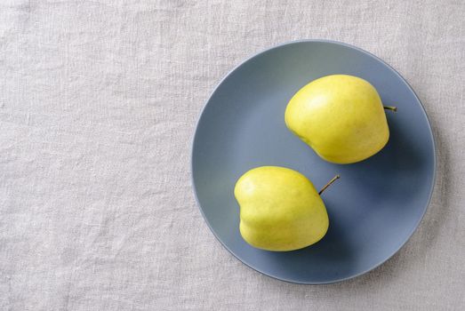 Ugly fresh food concept with fresh misshapen golden apples on a blue plate in a concept of aesthetic perceptions of food, top down on white with copy space