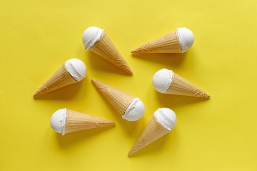 Group of six cones with creamy vanilla ice cream or gelato on a vivid yellow background arranged in the centre