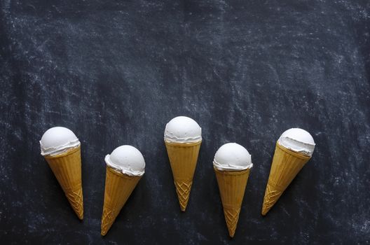 Border of five ice cream cones with delicious creamy vanilla ice-cream arranged on a textured dark grey background with copy space