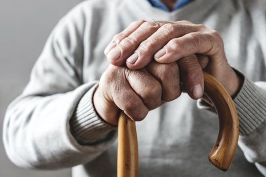 Close up details of the folded hands of an elderly man resting on a walking cane in a mobility and health concept