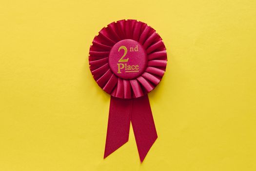 2nd Place red winners ribbon rosette on a colorful yellow background with copy space on either side