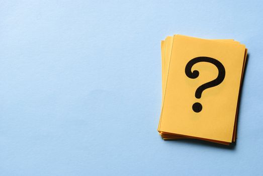 Stack of question marks on yellow cards arranged to the side on blue background with copy space