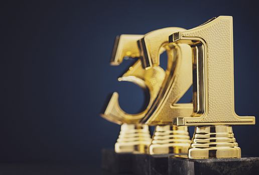 Close up view of three separate slightly blurry golden number trophies in front of dark blue gradient background