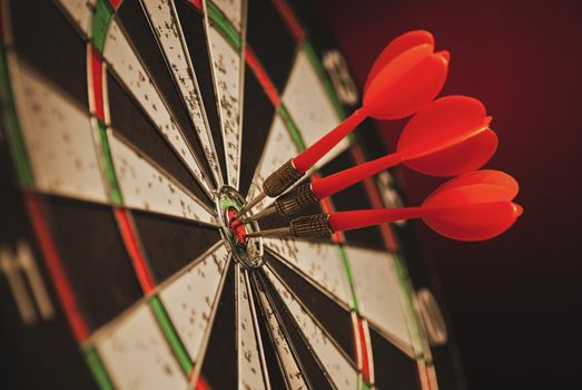 Three darts in the center bulls eye of a target clustered together in a conceptual image over a dark background