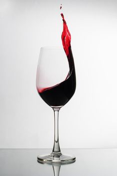 Red wine splashing up the side of a wineglass in a freeze motion conceptual image over a reflective white surface