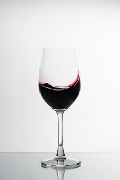Rich deep red wine swirled in an elegant wine glass on a reflective surface against a white background with copy space conceptual of viticulture and fine dining