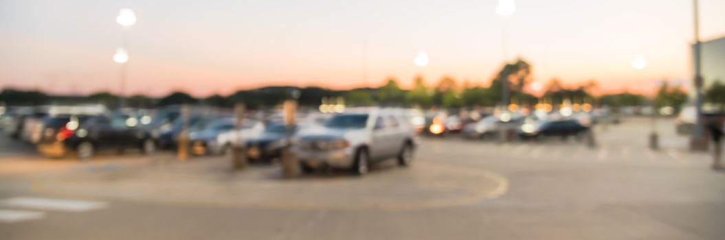 Panorama view abstract blurred parking lot of modern shopping center in Houston, Texas, USA. Exterior mall complex with row of cars in outdoor uncovered parking, bokeh light poles in background