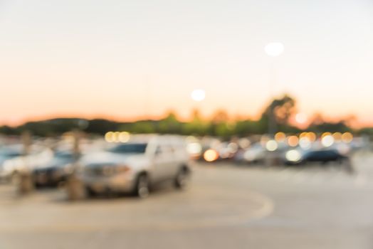 Abstract blurred parking lot of modern shopping center in Houston, Texas, USA. Exterior view mall complex with row of cars in outdoor uncovered parking, bokeh light poles in background