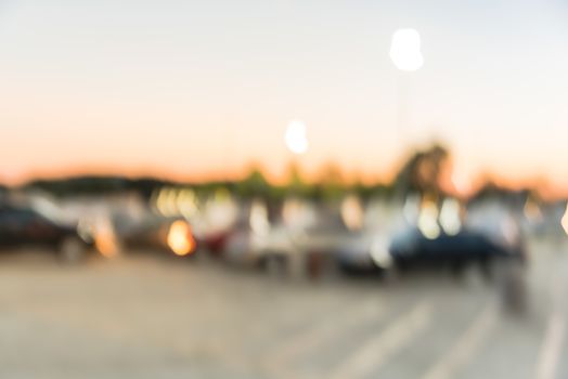 Abstract blurred parking lot of modern shopping center in Houston, Texas, USA. Exterior view mall complex with row of cars in outdoor uncovered parking, bokeh light poles in background