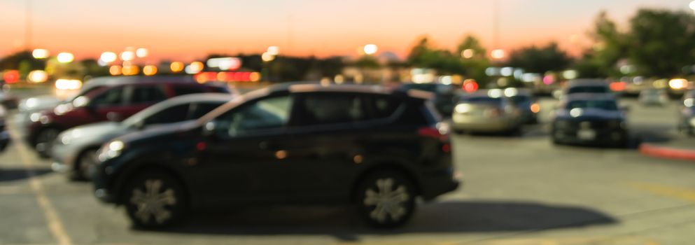 Panorama view abstract blurred parking lot of modern shopping center in Houston, Texas, USA. Exterior mall complex with row of cars in outdoor uncovered parking, bokeh light poles in background