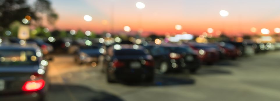 Panorama view abstract blurred parking lot of modern shopping center in Houston, Texas, USA. Exterior mall complex with row of cars in outdoor uncovered parking, bokeh light poles in background
